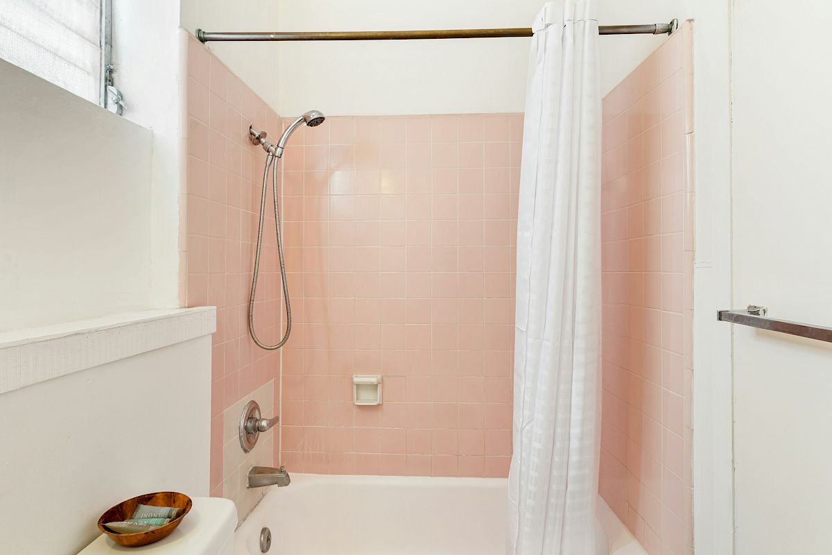 A bathroom bathtub with pink tile walls, a chrome showerhead, and a white shower curtain hanging down.