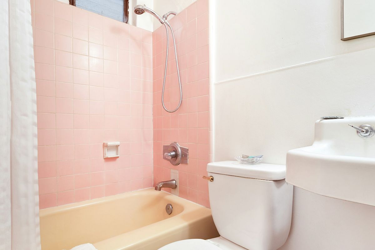 A bathroom with pink tiled shower and a chrome showerhead, plus a white toilet nearby.