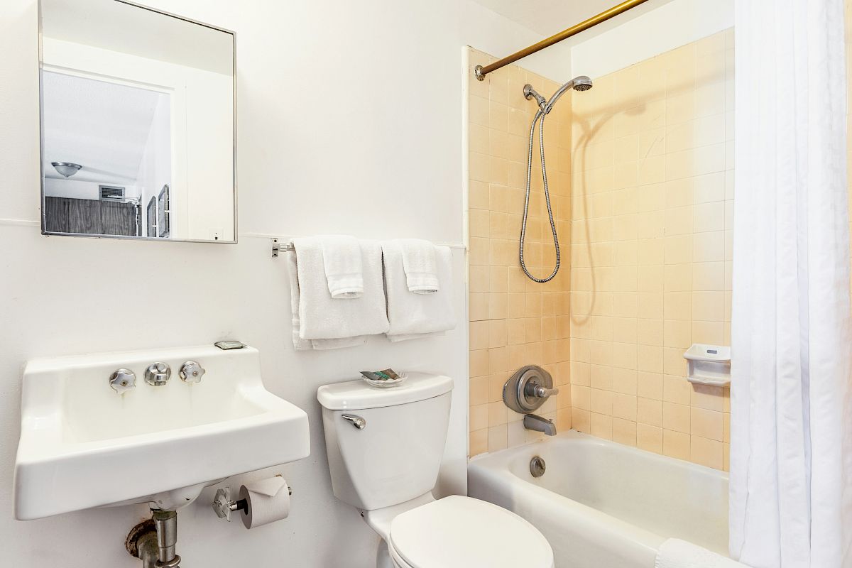 A clean bathroom with sink, toilet, and a tub/shower with white curtain and towel.