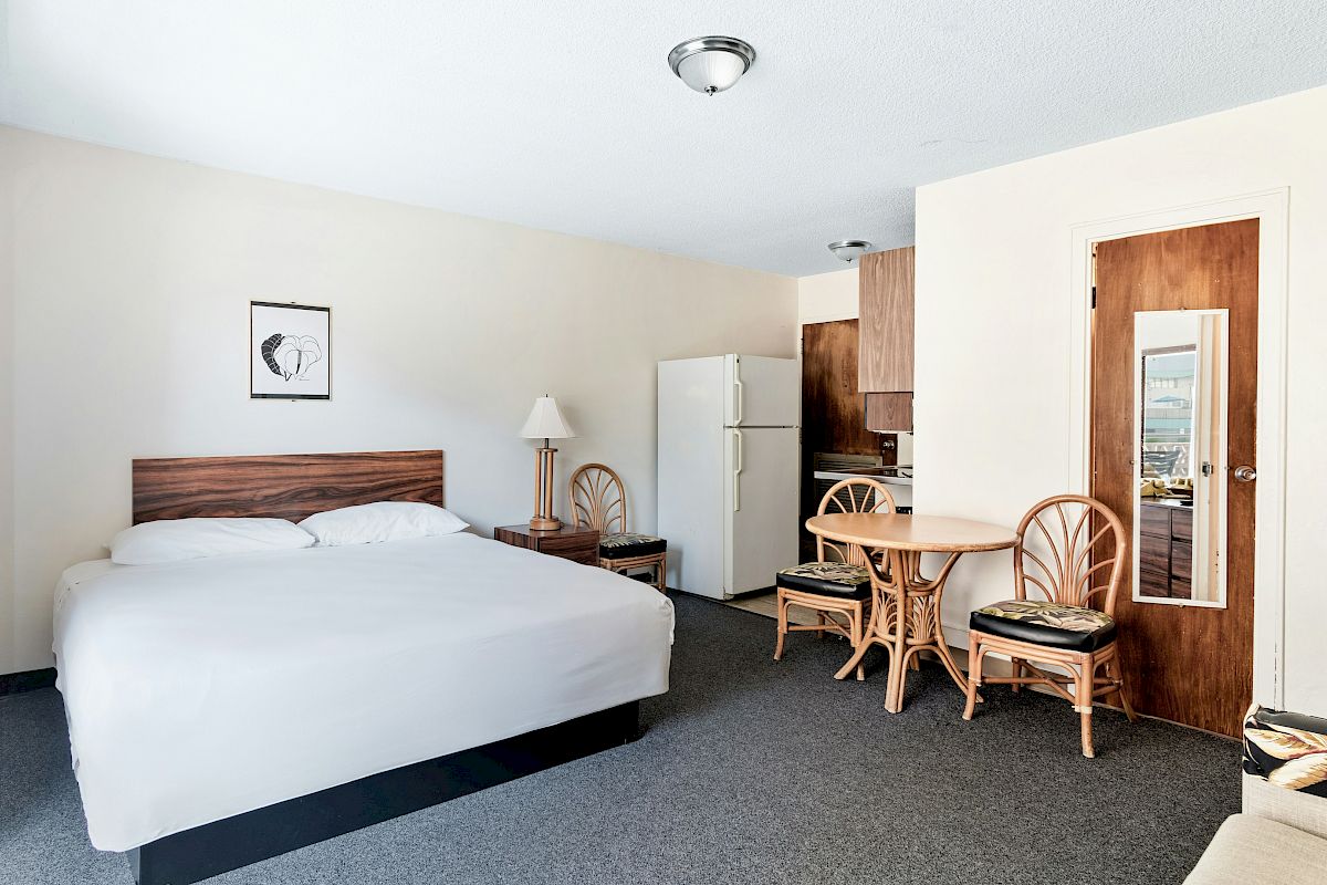 A hotel room with a bed, table and chairs, kitchenette area, and ceiling light.