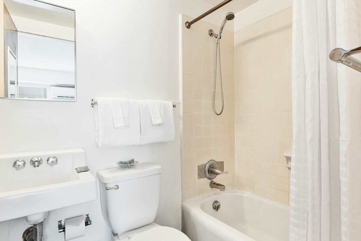 A bright bathroom with a toilet, bathtub with shower, towel rail, and a sink vanity.