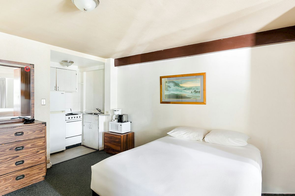 A hotel room with a double bed, dresser, wall art, and a small kitchenette with stove and appliances.