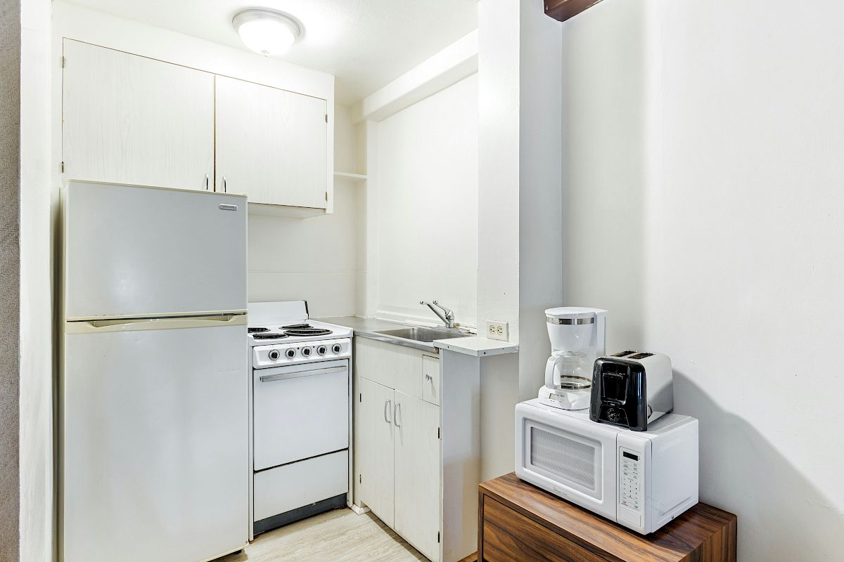 A bright small kitchen with a refrigerator, electric stove, sink, and countertop coffee maker and microwave.