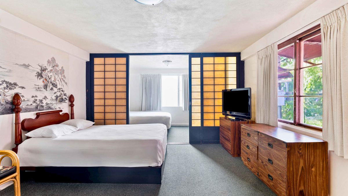 The image shows a bedroom with two beds, a dresser, a TV, sliding shoji screens, and a window with curtains.