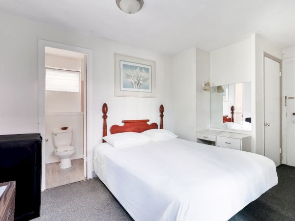 A small hotel room with a double bed, bedside table, wall mirror, and an adjoining bathroom visible through an open door.