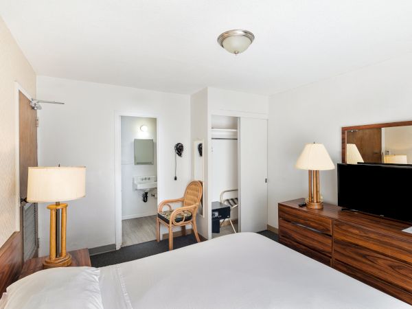 A hotel room with a bed, lamps, a TV, and a chair near an open closet and bathroom door.