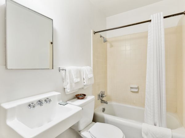 A clean, white bathroom with a sink, mirror, toilet, and a bathtub with a shower curtain. Towels are hung by the sink.