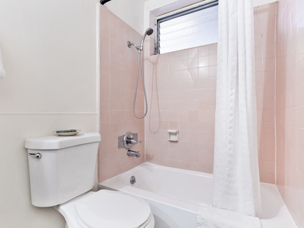 A bathroom with pink tiled walls, a showerhead, a bathtub, a toilet, and a white shower curtain is shown.