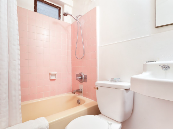 A small bathroom with pink tiles, a bathtub, shower, toilet, and sink; white walls and shower curtain.