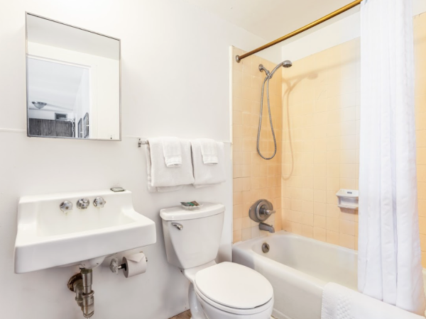 A clean bathroom with a sink, mirror, toilet, and shower-tub combo with a white curtain and beige tiles.