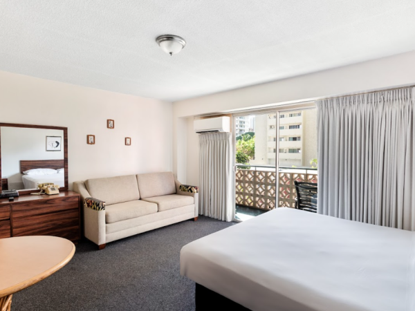 A hotel room with a bed, sofa, TV, and a balcony with sliding doors and curtains.