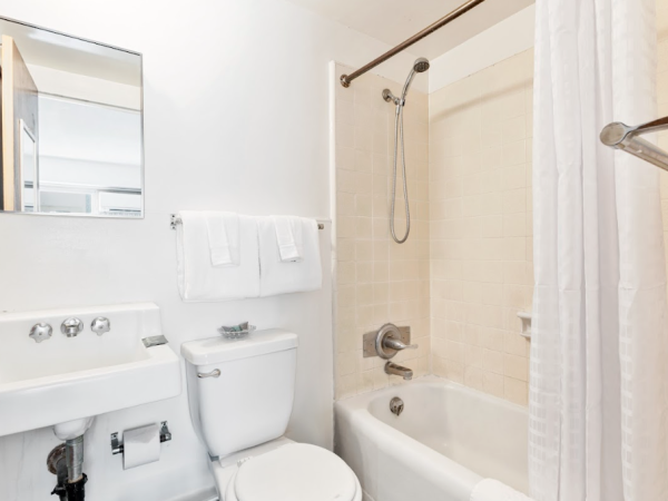 A white bathroom with a toilet, sink, and bathtub with a shower curtain. Towels hang above the toilet on a rack.