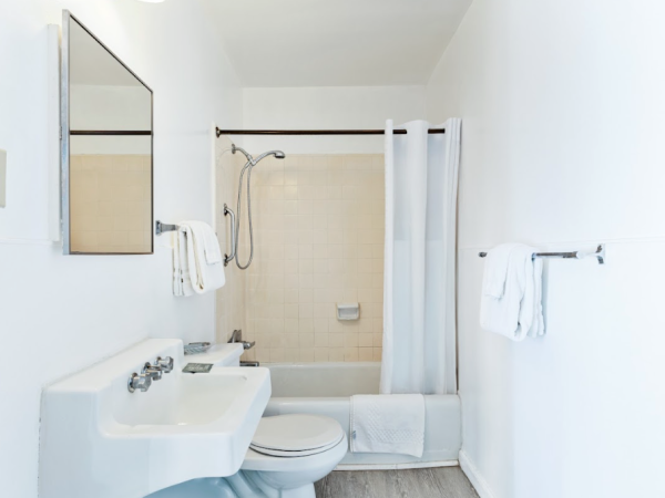 A clean bathroom with a sink, toilet, and bathtub. White tiles, a mirror, and towel racks are visible.