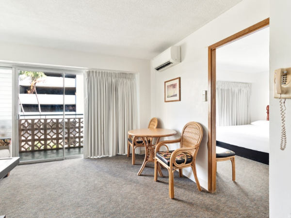 A room with a table, two chairs, a bed, and a balcony door. Walls are white, and there's a phone on the wall.