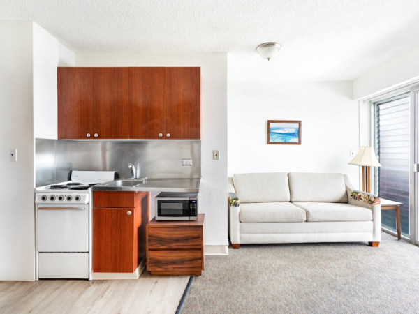 A compact living space with a kitchenette, sofa, and a sliding door leading outside.