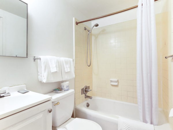 A clean, white bathroom with a shower, bathtub, toilet, sink, and towels. A mirror and shower curtain are also visible.