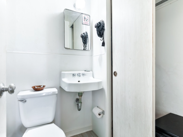 A small bathroom with a toilet, sink, mirror, and hairdryer on the wall. There's a sliding door and a black mat or object nearby.