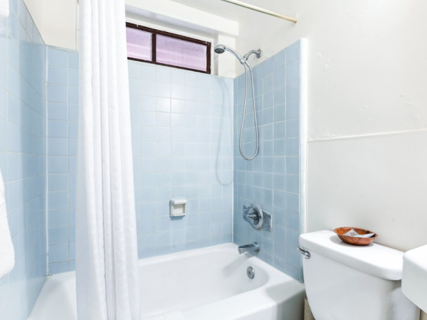 A bathroom with a blue-tiled bathtub and shower, white curtain, toilet, and a small window above the shower.