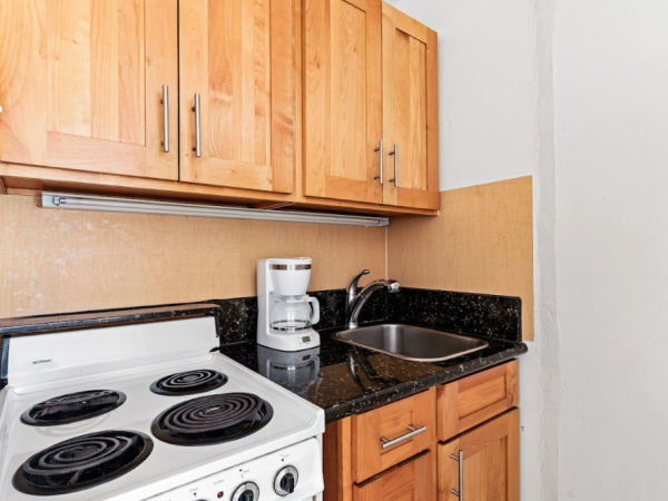 A small kitchen features a stovetop, wooden cabinets, a coffee maker on a countertop, and a sink with a faucet.