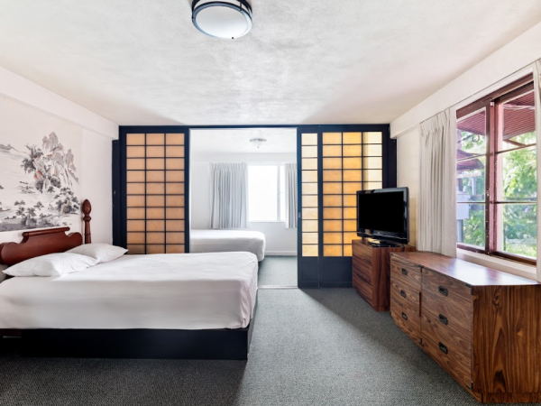 The image shows a bright bedroom with a bed, a dresser, a TV, and large windows, featuring a sliding shoji screen partition.