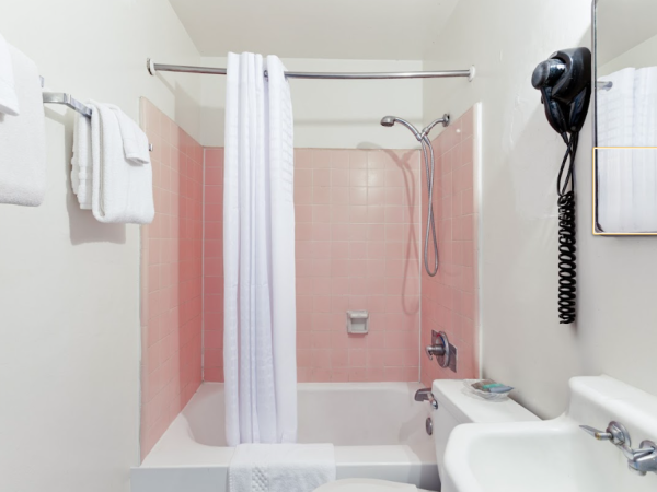 The image shows a bathroom with a pink-tiled shower, white curtain, towels, sink, and wall-mounted hairdryer.