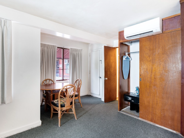 The image shows a room with a table and chairs near a window, curtains, a built-in closet with a mirror, and an air conditioning unit on the wall.