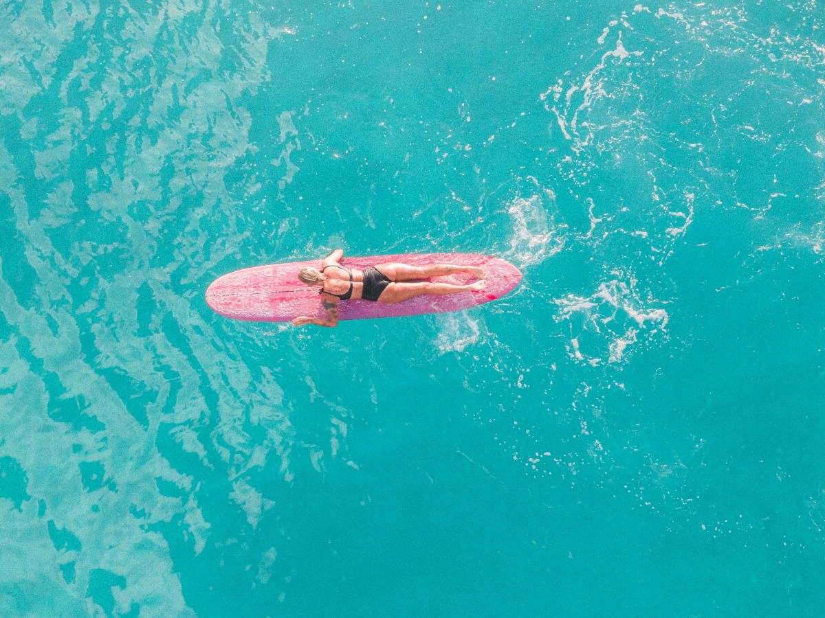 A person paddles a pink board on bright turquoise water, gliding calmly across the ocean.