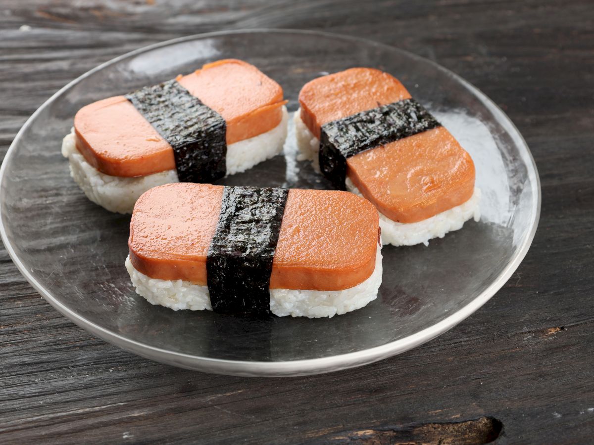 Three salmon nigiri sushi pieces arranged on a clear plate, each topped with a strip of nori wrapping around the rice.