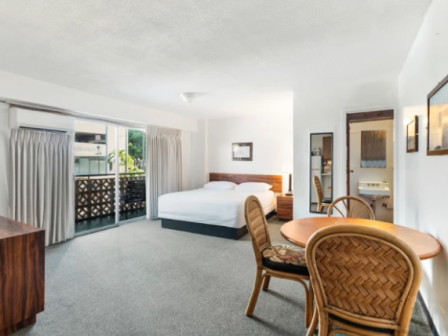 A hotel room with a bed, seating area, round dining table, wicker chairs, a balcony with lattice, and a desk; spacious and bright.