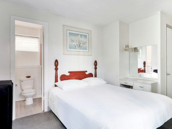 A bright bedroom with a double bed, framed wall art, a vanity mirror, and an adjoining bathroom with a toilet.