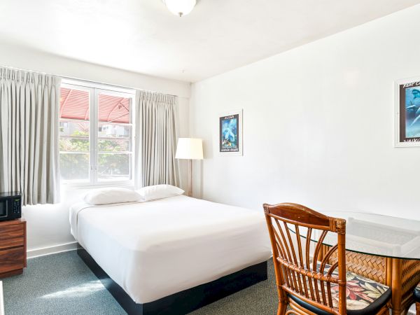 A bright hotel bedroom with a single bed, curtains, window, microwave, lamp, and ocean-themed wall art.
